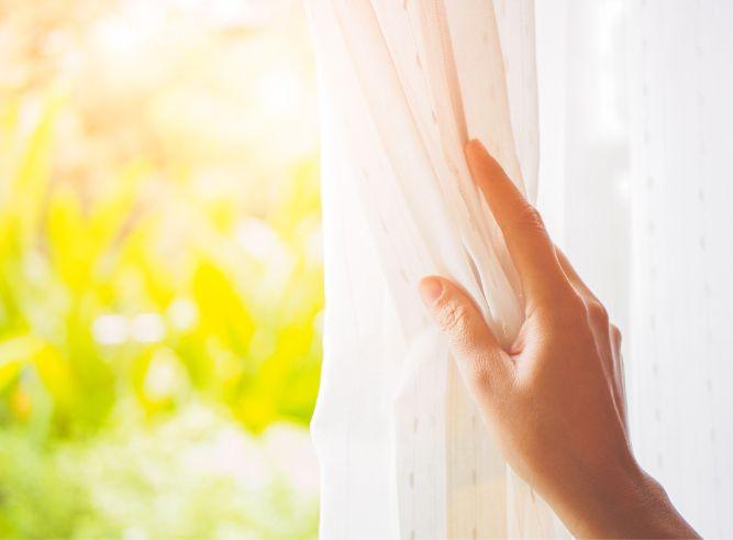 Woman's hand opening curtains in the bedroom with natural light — Photo